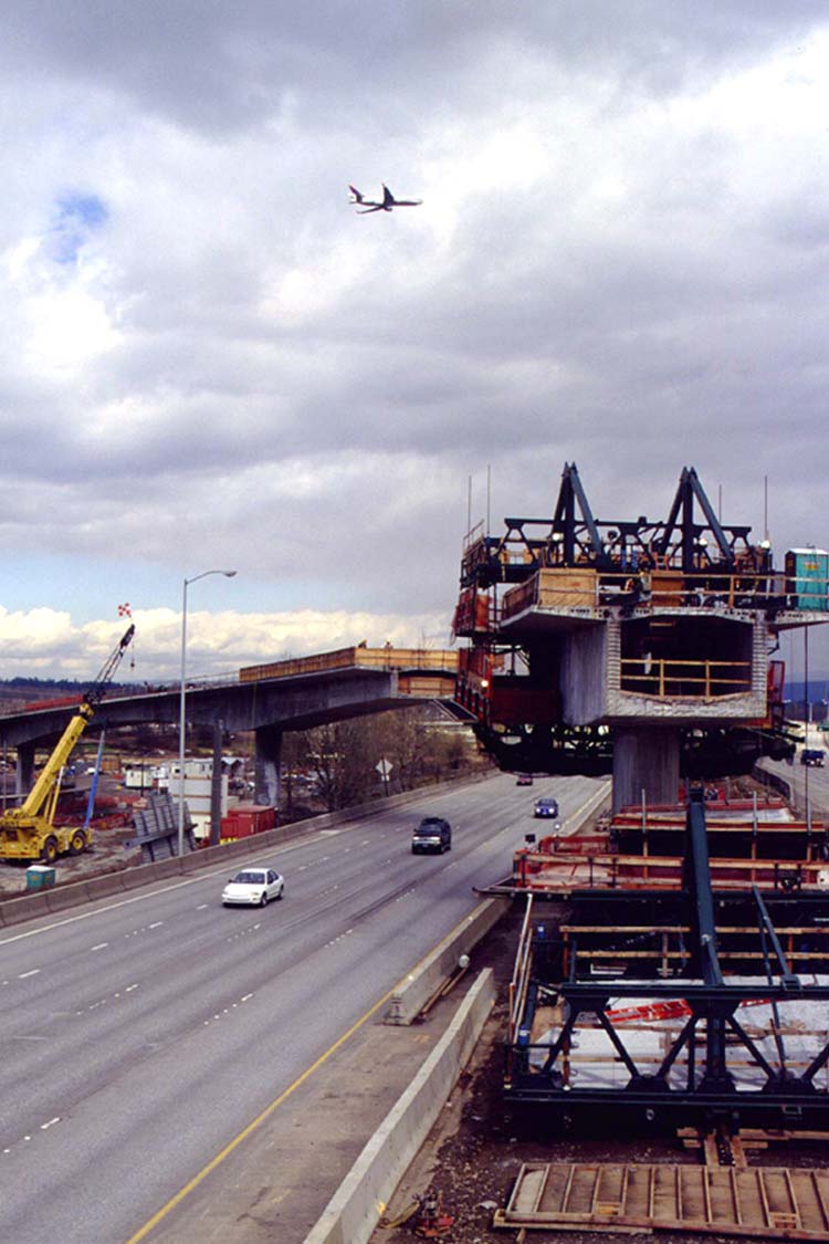 Construction of the Airport MAX Red Line over the I-205 freeway facing north with a plane overhead